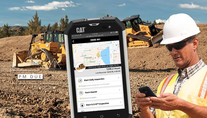 A person holding a handheld device on displaying the Cat app with two Cat dozers behind him