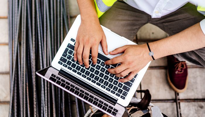 A person wearing a safety vest typing on a laptop